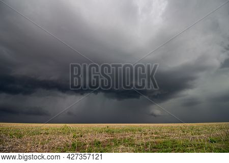 A Dark Storm Cloud Looms On The Horizon, Bringing Rain To A Farmer's Field.