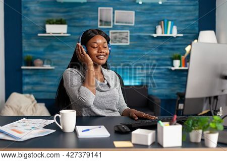 African American Student Wearing Headphones Listening Happy Music Sitting At Desk In Living Room. Wo