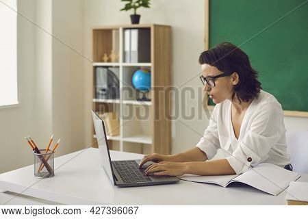 Young Woman Teacher Working Online On Laptop In Classroom