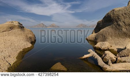 Landscape View Of Driftwood And Rocks In The Foreground With Distant Mountains And Clouds With Patte