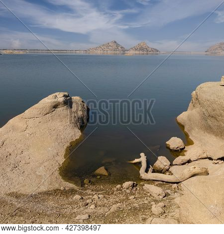 A Landscape View of driftwood and rocks in the foreground and distant mountains and clouds with patt