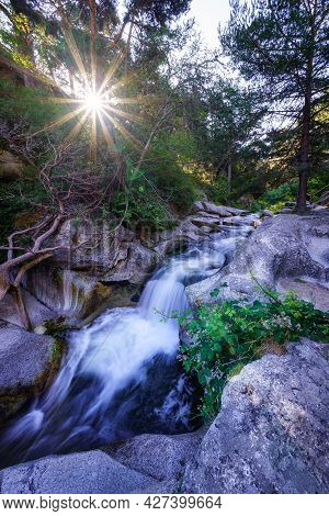Small Stream Between Rocks With Sunlight Coming Out Between The Trees.
