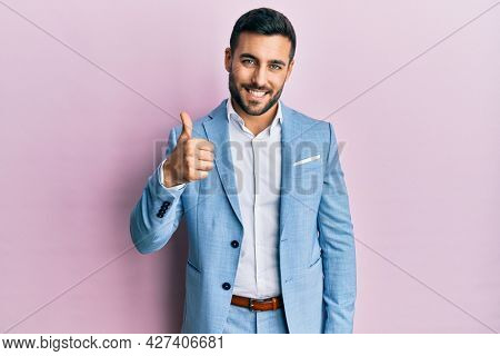Young hispanic businessman wearing business jacket doing happy thumbs up gesture with hand. approving expression looking at the camera showing success. 