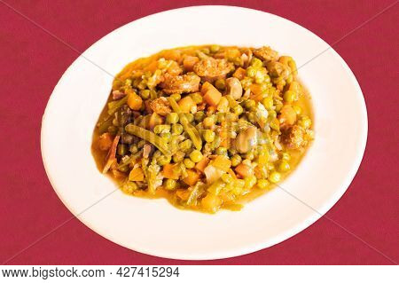 White Kitchen Dish Of Vegetable Stew With Legumes Such As Peas, Carrots, Abas And Chorizo On A Red C