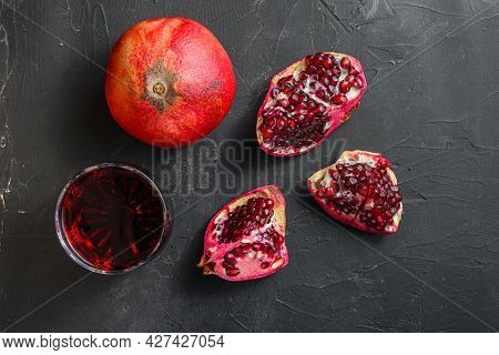 Garnet Juice In Glass With Cuts And Whole Pomegranate Over  Black Textured Background, Top View