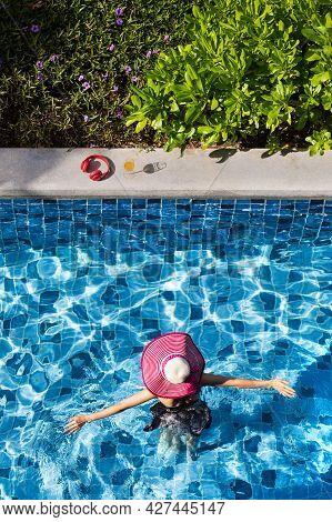 Woman Wear Big Hat Spread Arms And Walking In Swimming Pool Going To Glass Of Orange Juice And Red H