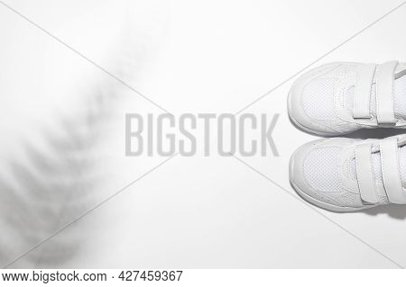 Flat Lay Two White Child Sneakers With Velcro Fasteners With Shadows From A Fern Or Palm Tree Isolat