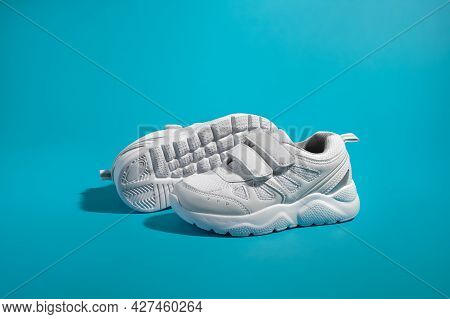 Side View Of One White Unisex Sneaker With Velcro Fasteners Standing In Front Of The Sole Of Another