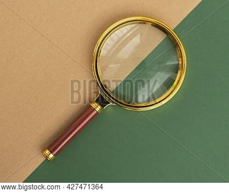 Magnifier On Green And Brown Carton Background. Concept Of Searching And Investigating.