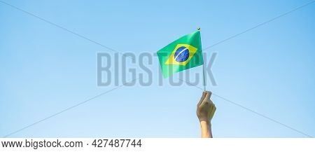 Hand Holding Brazil Flag On Blue Sky Background. September Independence Day And Happy Celebration Co