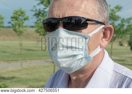 Man Wearing Sunglasses And A Medical Mask. Close-up, Blurry Background. Stock Photo