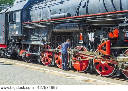 Worker Checks A Black Retro Steam Locomotive At Railway Station
