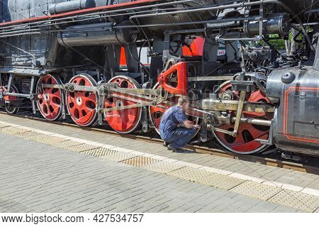 Worker Checks A Black Retro Steam Locomotive At Railway Station