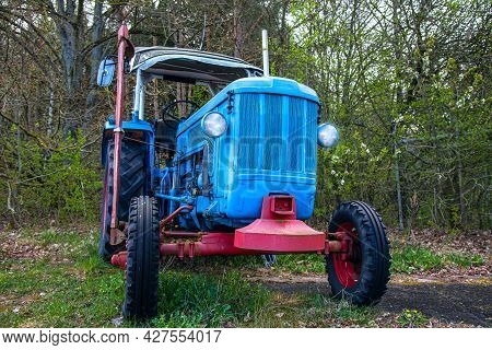 Blue Tractor Old On The Background Of Trees In Spring