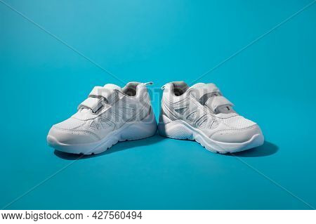 Front View Of Two White Unisex Sneakers With Velcro Fasteners Facing In Different Directions On A Bl