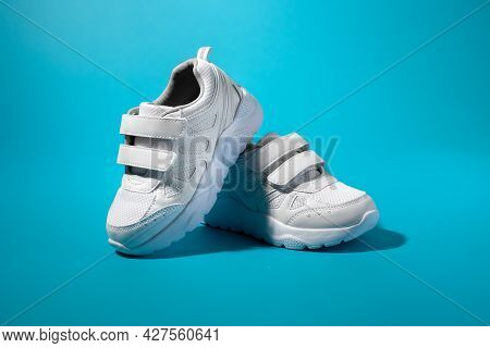 One White Childrens Running Shoe Stands On The Back Of Another Running Shoe On A Blue Paper Backgrou