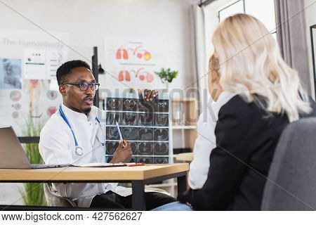 Competent African Doctor In Eyglasses And Lab Coat Showing And Explaining X Ray Results Of Little Bo