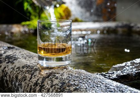 Glass Of Strong Scotch Single Malt Whisky Served On Old Stone Reservoir For Water From Mountain Spri