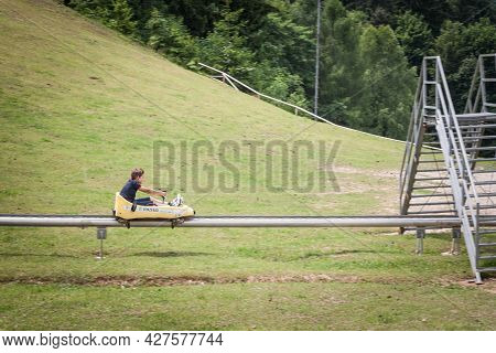 Bled, Slovenia - June 12, 2021: Boy, A Kid, Going Down A Slope Of Straza Bled With A Bobsled On A Su