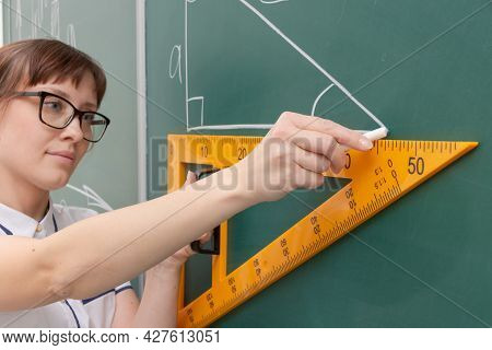 School Teacher Young Woman In The Class At The Blackboard Draws A Triangle With A Ruler. Portrait. C