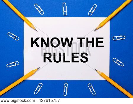 On A Blue Background, White Paper Clips, Yellow Pencils And A White Sheet Of Paper With The Text Kno