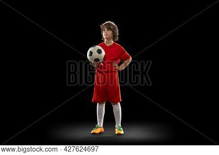 Portrait Of Little Boy, Football Soccer Player Posing With Football Ball Isolated On Dark Studio Bac