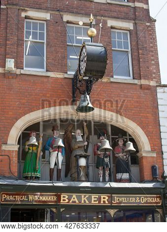 Five Figures, Including Old Father Time And A British Soldier All In Tradition Dress Above A Shop In