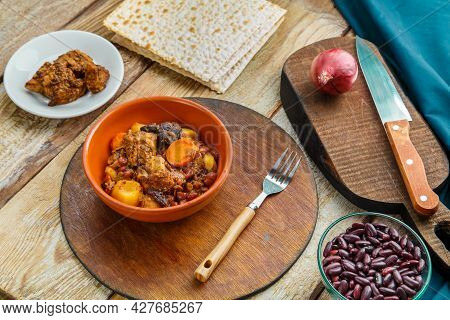 Jewish Dish Chelnt With Meat On The Table In A Plate On A Stand Next To The Ingredients And Matzo. H