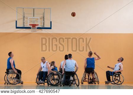 Disabled War veterans mixed race opposing basketball teams in wheelchairs photographed in action while playing an important match in a modern hall. 