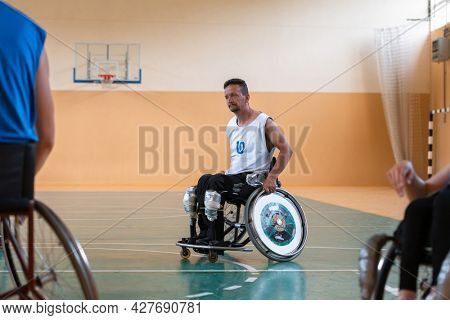 Disabled War veterans mixed race opposing basketball teams in wheelchairs photographed in action while playing an important match in a modern hall. 