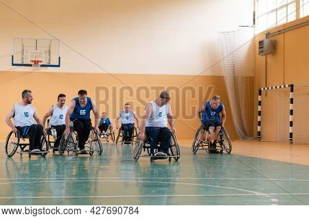 Disabled War veterans mixed race opposing basketball teams in wheelchairs photographed in action while playing an important match in a modern hall. 