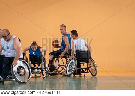 Disabled War veterans mixed race opposing basketball teams in wheelchairs photographed in action while playing an important match in a modern hall. 