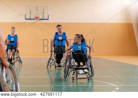 Disabled War veterans mixed race opposing basketball teams in wheelchairs photographed in action while playing an important match in a modern hall. 