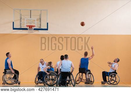 Disabled War veterans mixed race opposing basketball teams in wheelchairs photographed in action while playing an important match in a modern hall. 