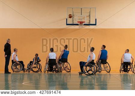 Disabled War veterans mixed race opposing basketball teams in wheelchairs photographed in action while playing an important match in a modern hall. 