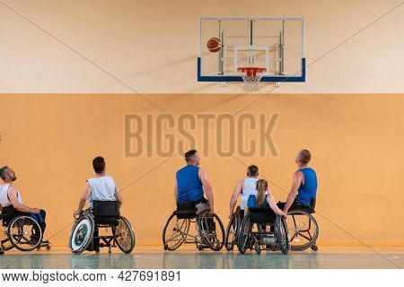 Disabled War veterans mixed race opposing basketball teams in wheelchairs photographed in action while playing an important match in a modern hall. 