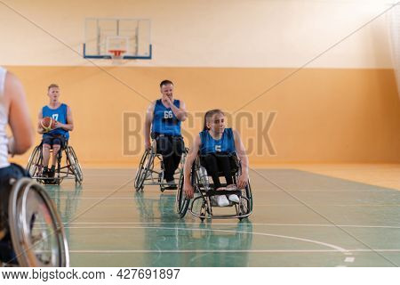 Disabled War veterans mixed race opposing basketball teams in wheelchairs photographed in action while playing an important match in a modern hall. 