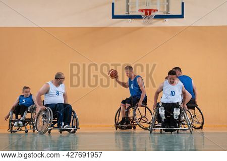 Disabled War veterans mixed race opposing basketball teams in wheelchairs photographed in action while playing an important match in a modern hall. 