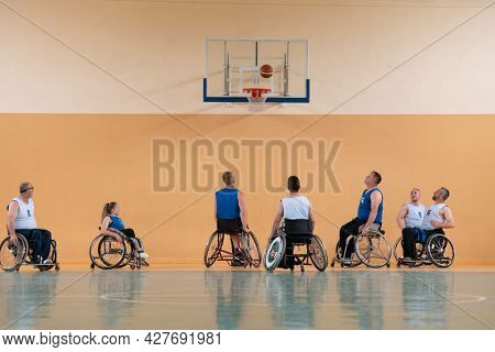 Disabled War veterans mixed race opposing basketball teams in wheelchairs photographed in action while playing an important match in a modern hall. 