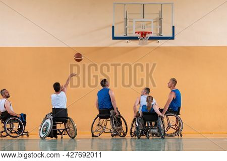 Disabled War veterans mixed race opposing basketball teams in wheelchairs photographed in action while playing an important match in a modern hall. 