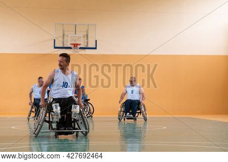 Disabled War veterans mixed race opposing basketball teams in wheelchairs photographed in action while playing an important match in a modern hall. 