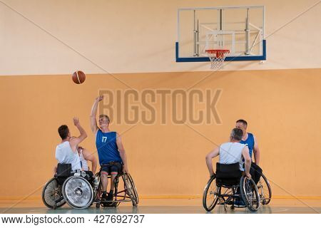 Disabled War veterans mixed race opposing basketball teams in wheelchairs photographed in action while playing an important match in a modern hall. 
