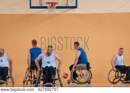 Disabled War veterans mixed race opposing basketball teams in wheelchairs photographed in action while playing an important match in a modern hall. 
