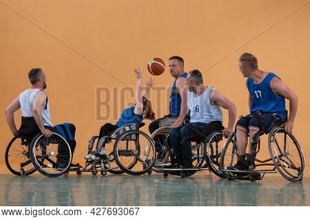 Disabled War veterans mixed race opposing basketball teams in wheelchairs photographed in action while playing an important match in a modern hall. 