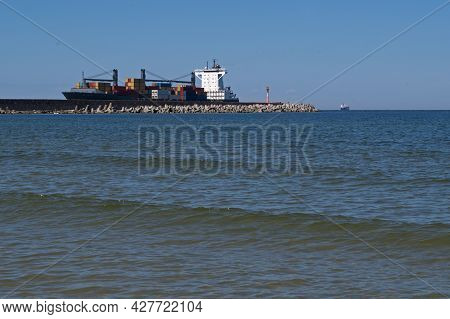 Blue Hulled Cargo Ship Loaded With Shipping Containers Of Various Colors Enters The Coastal Bay Past
