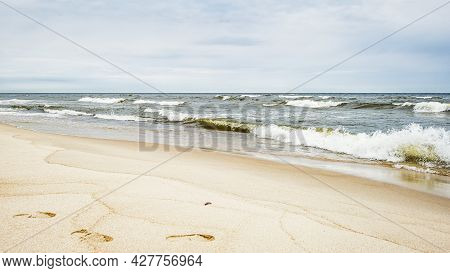 Sea Waves And Footprints On The Sand On The Beach And Overcast Sky