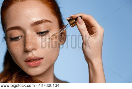 Beautiful Young Woman Apply Moisturizing Facial Serum Isolated On Blue Background. Morning Daily Bea