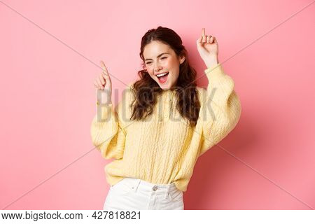 Happy Attractive Woman Having Fun, Pointing Fingers Up And Dancing Carefree, Smiling Upbeat, Standin