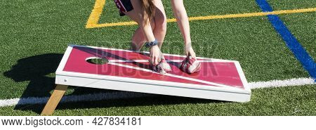 Horizontal View Of A Girl Picking Up Striped Bean Bags While Playing Cornhole On A Homemade Red And 