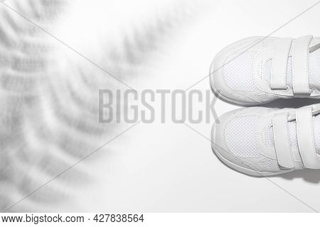 Flat Lay Two White Unisex Kid Sneakers With Velcro With Fern Or Palm Tree Shadows Isolated On A Whit